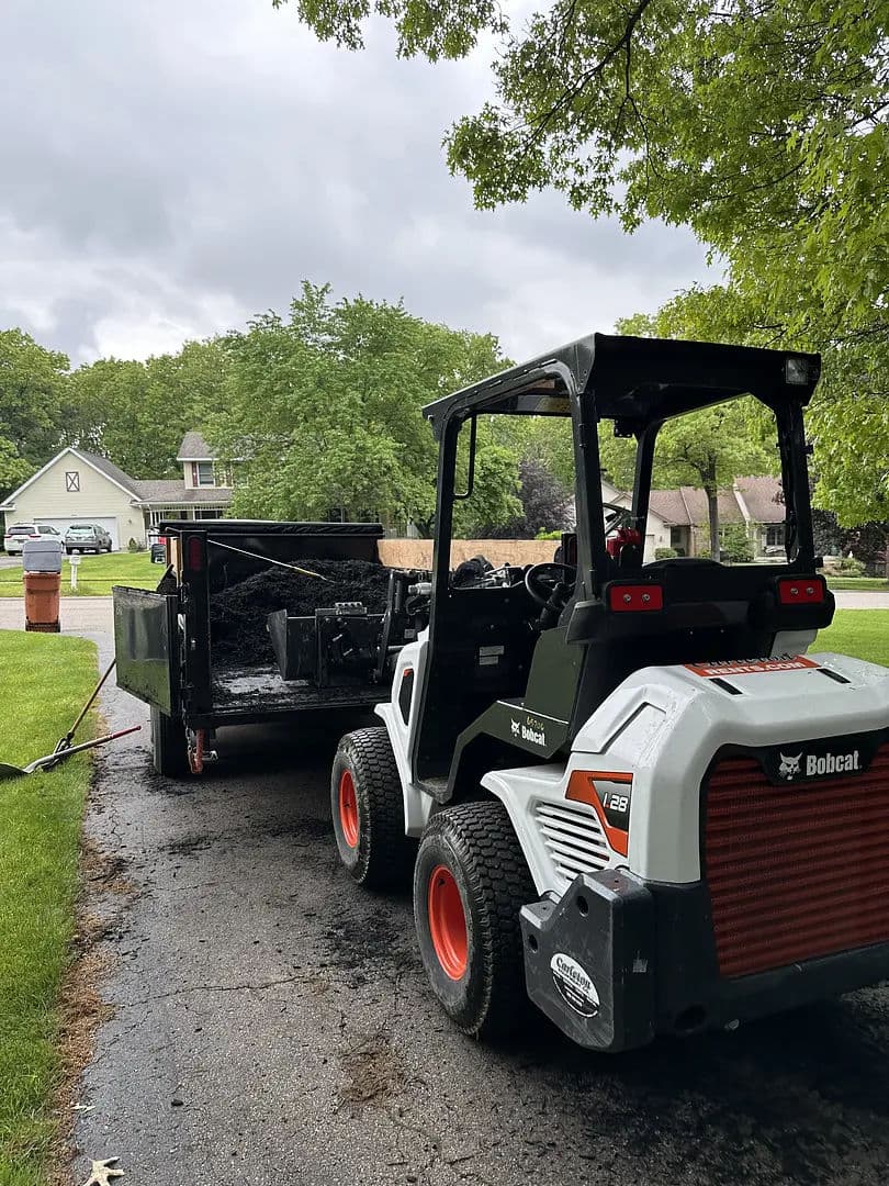 Bobcat F28 skid steer loader next to trailer, preparing for landscaping work outdoors.