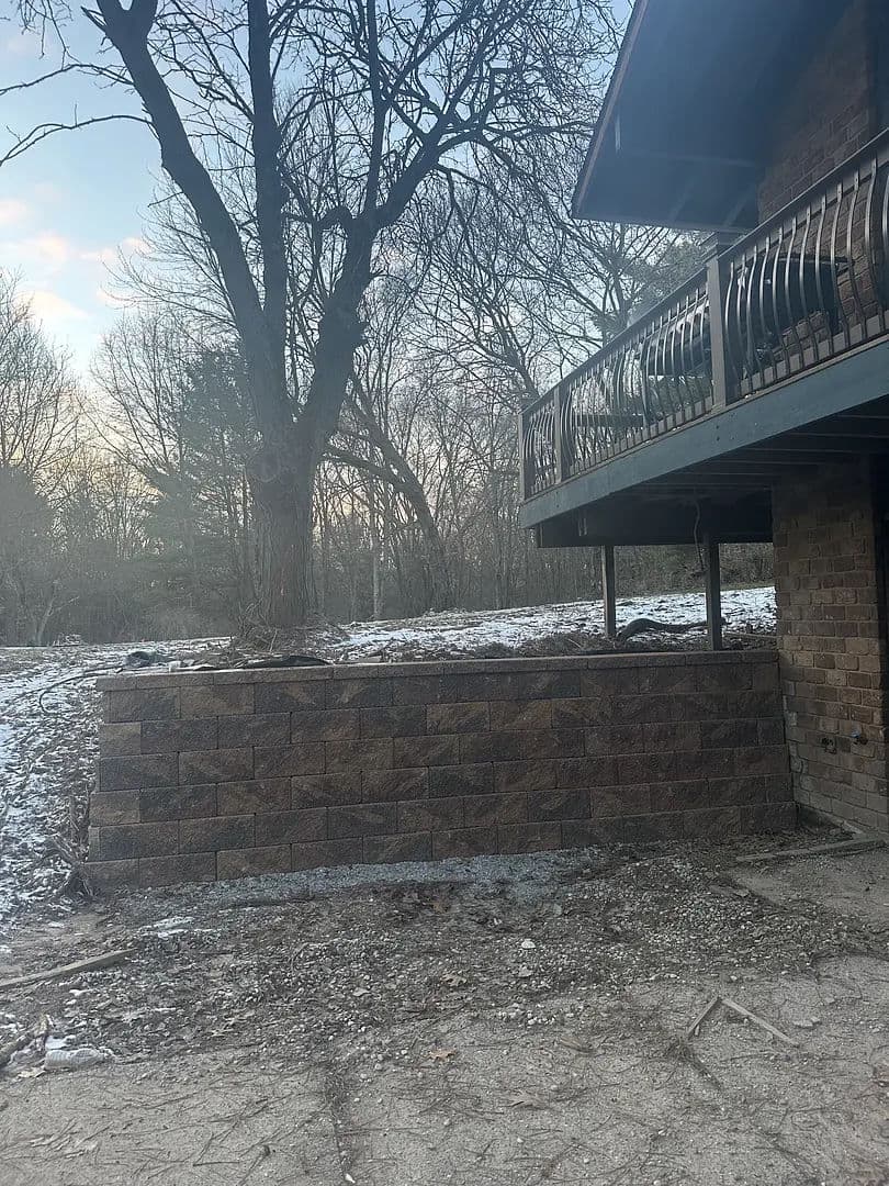Brick retaining wall beside a house with a balcony, surrounded by a snowy landscape.
