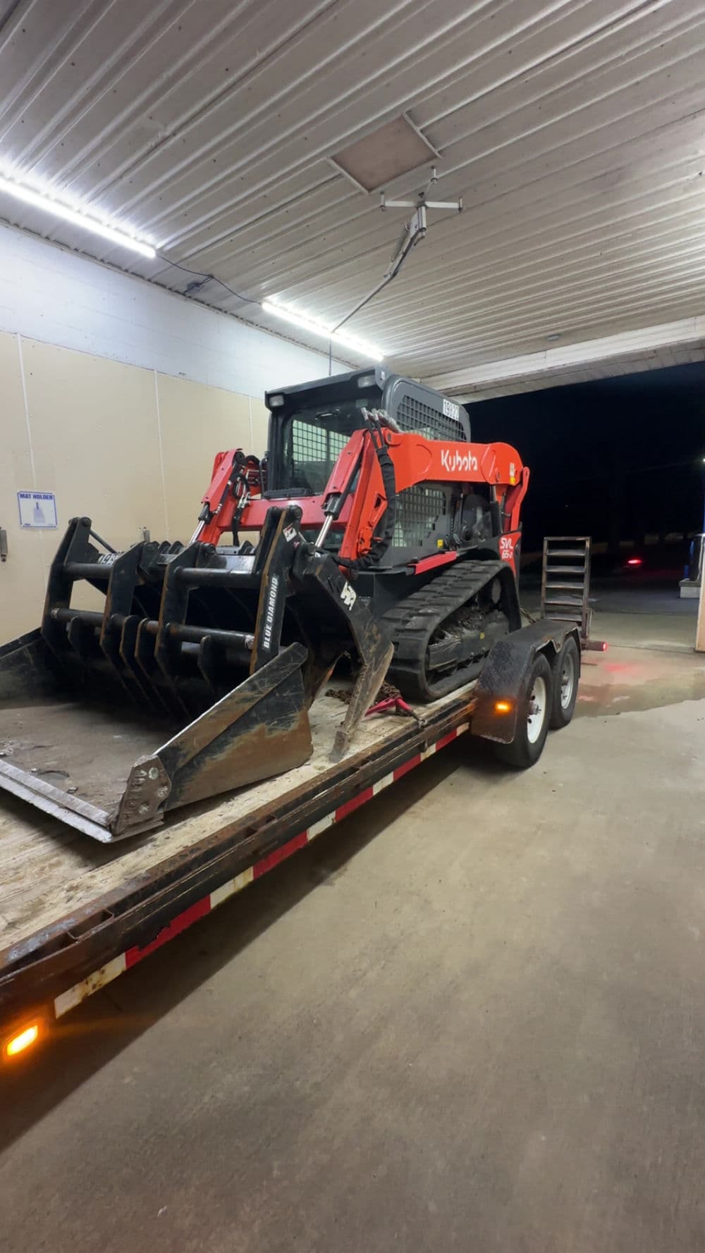 Kubota skid steer loader on a trailer, ready for transportation in a well-lit garage.