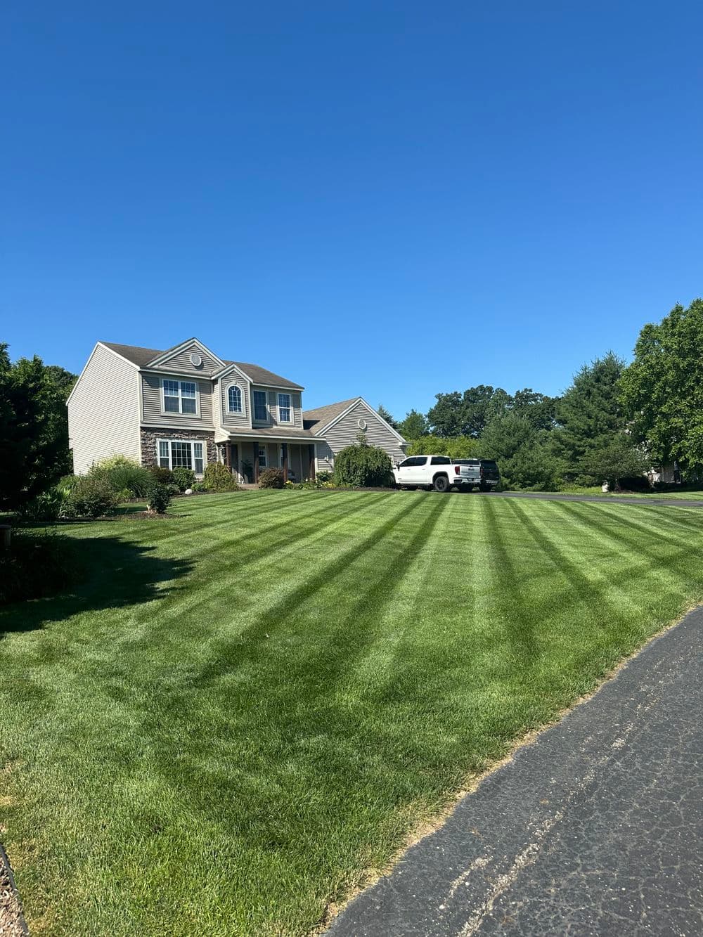 Two-story house with manicured lawn and a white SUV parked in the driveway under a clear blue sky.