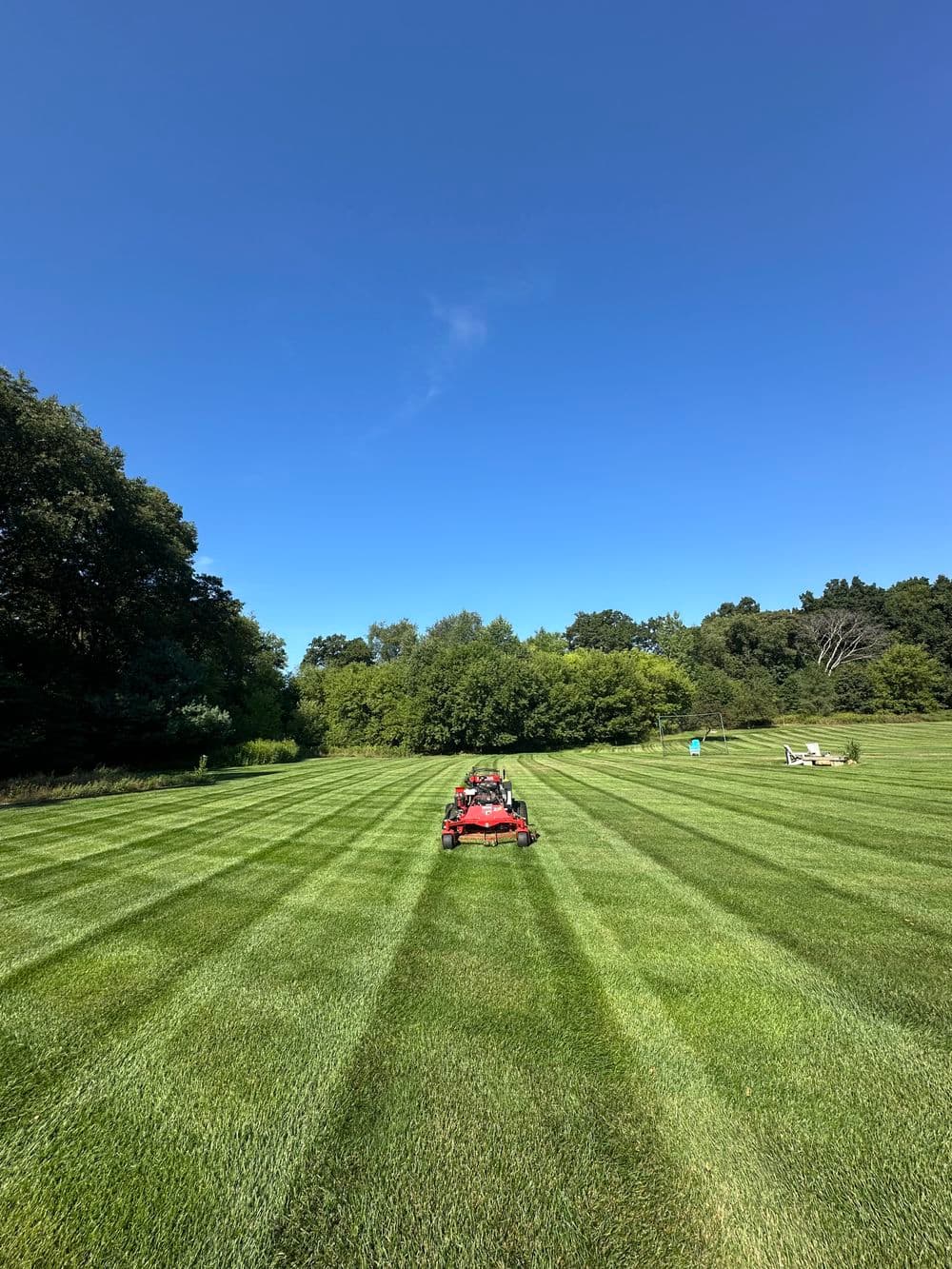 Red lawn mower on freshly mowed grass with clear blue sky in the background.